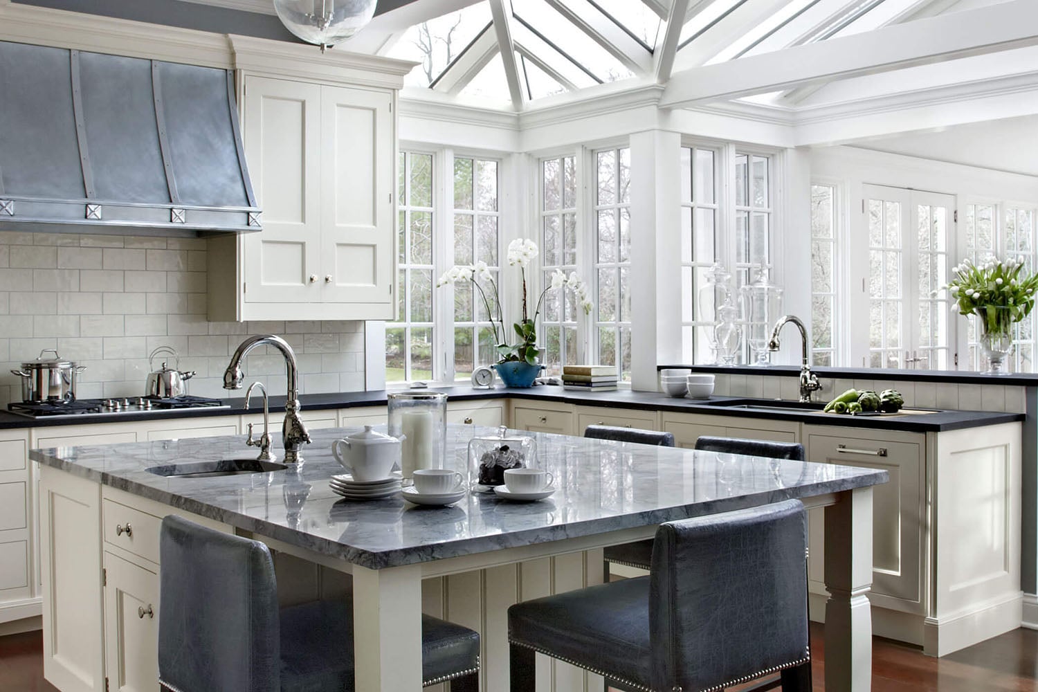 Coastal kitchen with warm wood flooring, white cabinets, and blue marble countertops.