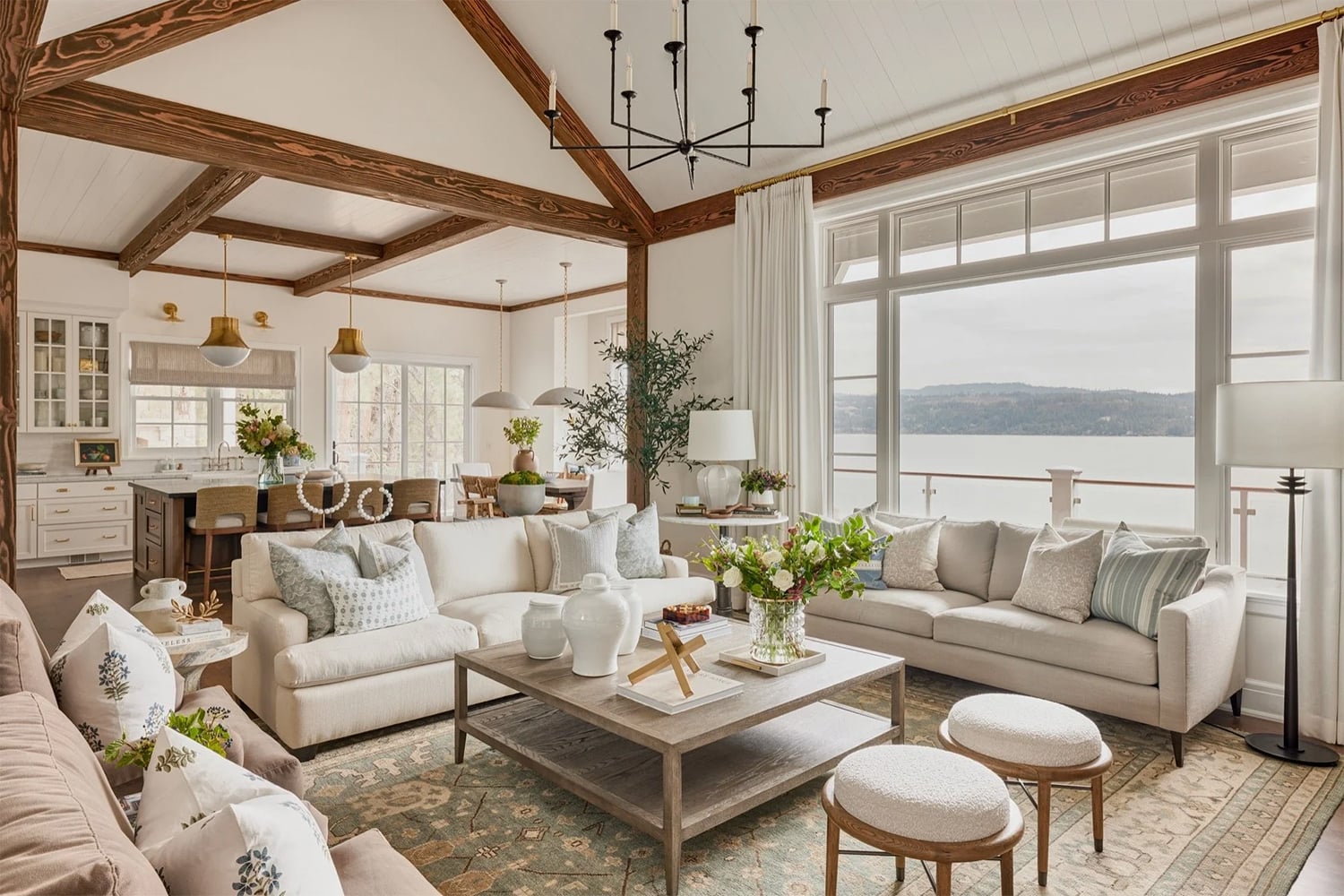 Open-concept coastal living room with wood ceiling beams, and natural sunlight.