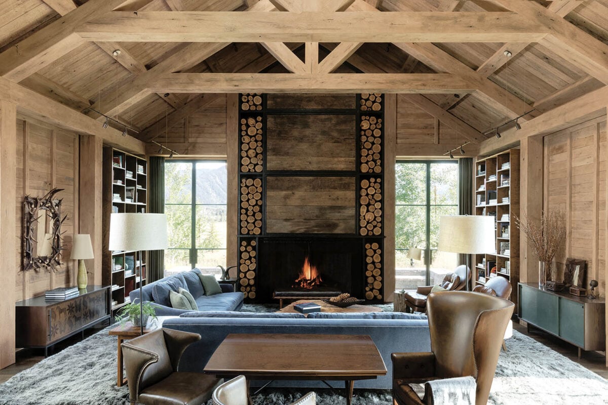 Traditional rustic living room with peaked wood ceiling, fireplace surround and wood paneled walls.