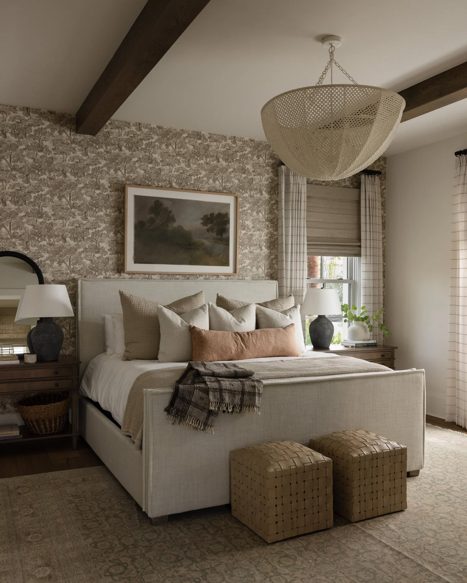 Moody farmhouse bedroom with a vintage landscape above the bed, and dark wood ceiling beams
