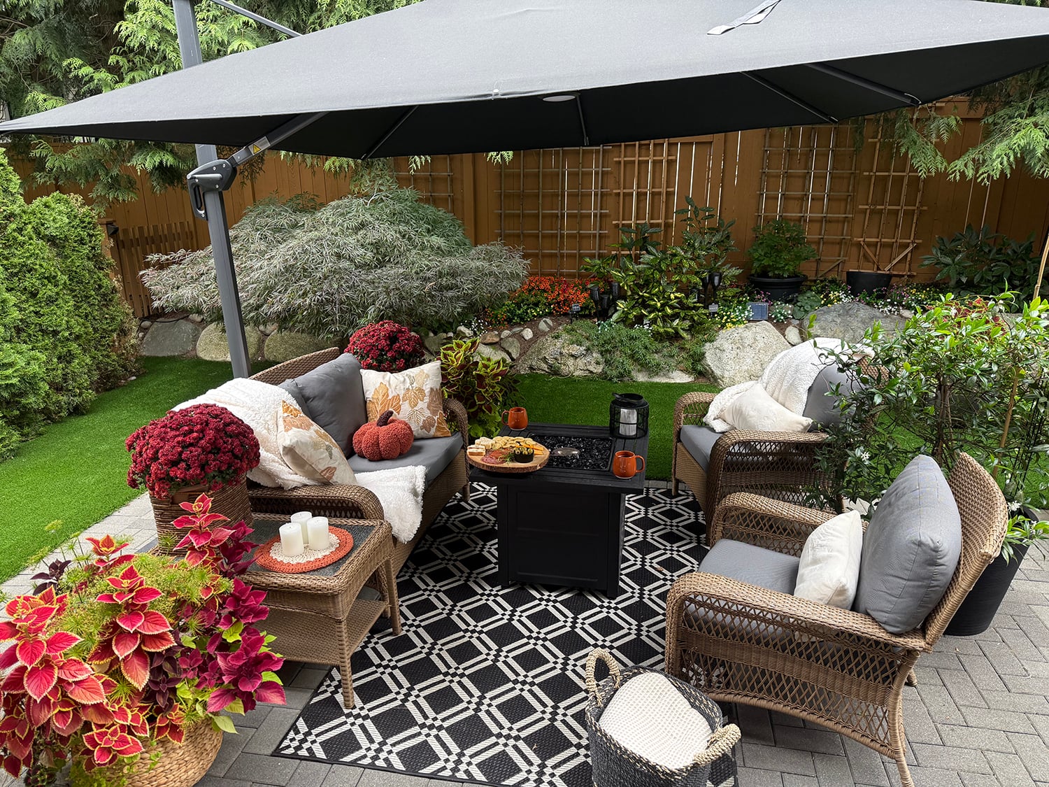 Modern rustic backyard decorated for fall with wicker sofa faux fur throws pumpkin pillows and coleus in woven baskets