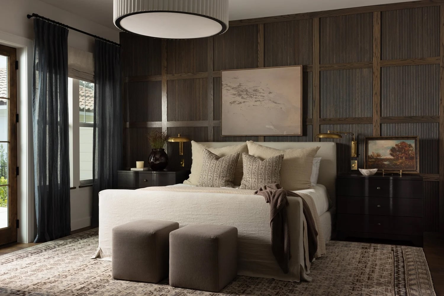 Modern farmhouse bedroom with dark wood flooring, wood accent wall and cream-toned bed.