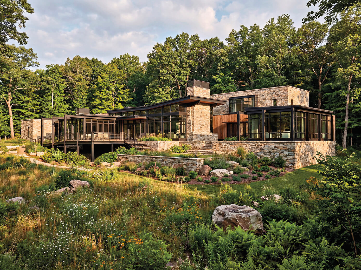 Exterior of a modern rustic home with large windows, cedar siding, and stone
