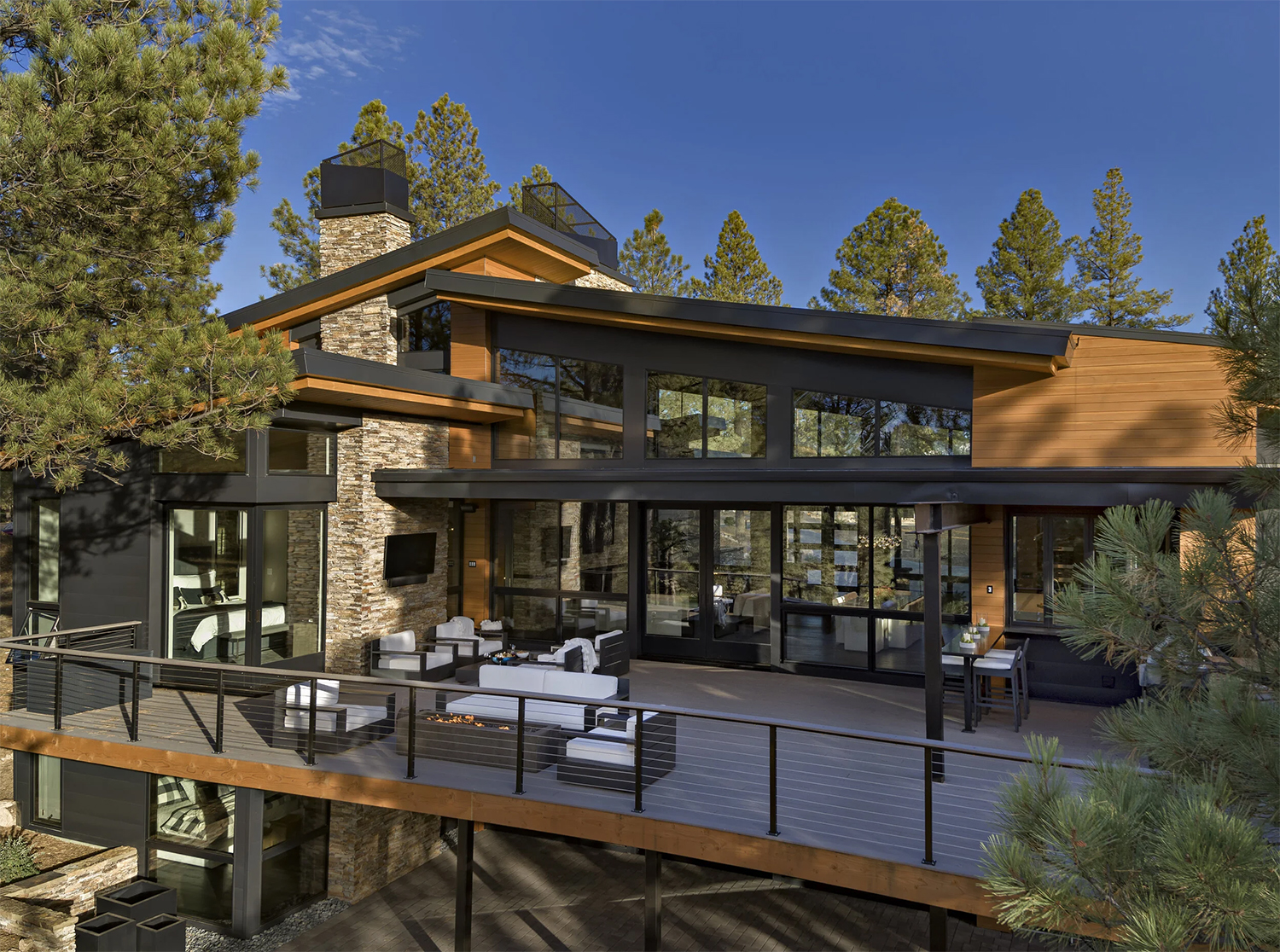 A modern mountain home with black metal used on roofline trim, window frames and deck railings