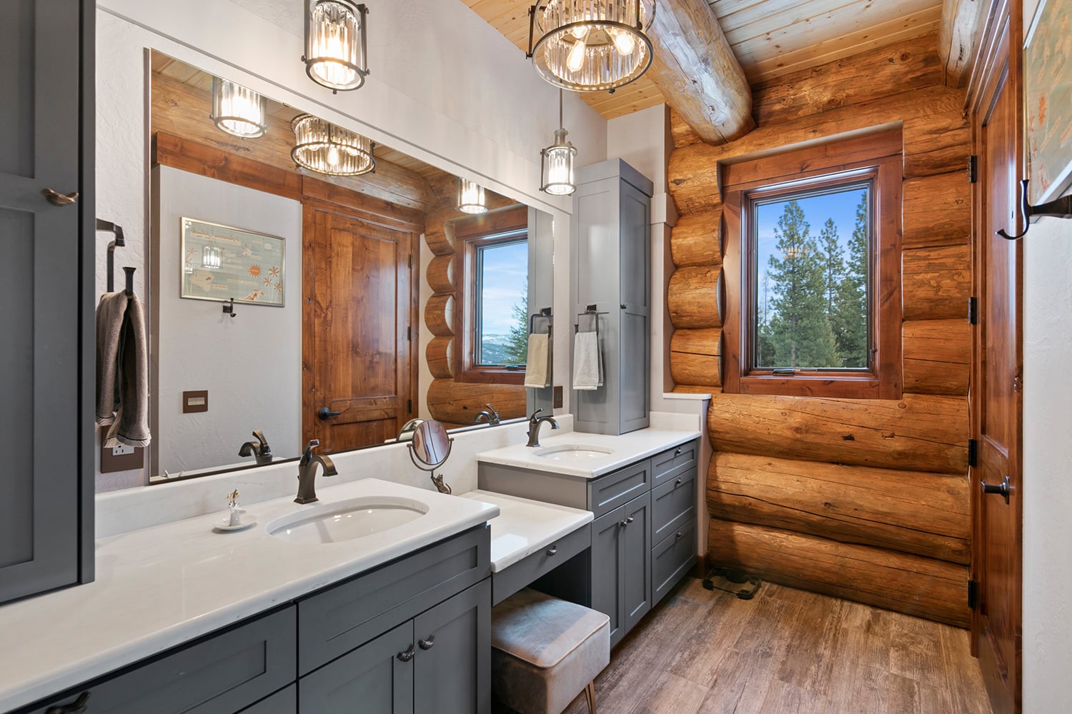 Rustic bathroom in a handcrafted log home with gray cabinets and white countertops.