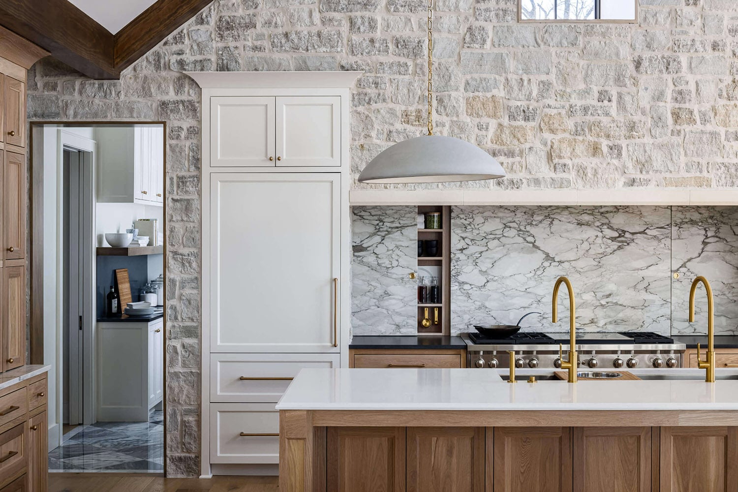Kitchen with natural stone accent wall, dramatically veined marble and white and light oak cabinets.