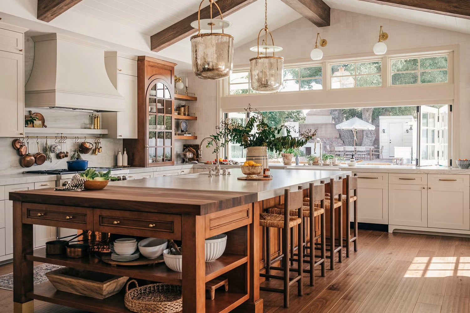 Country kitchen with warm white cabinets, wood island, and copper pot rack.