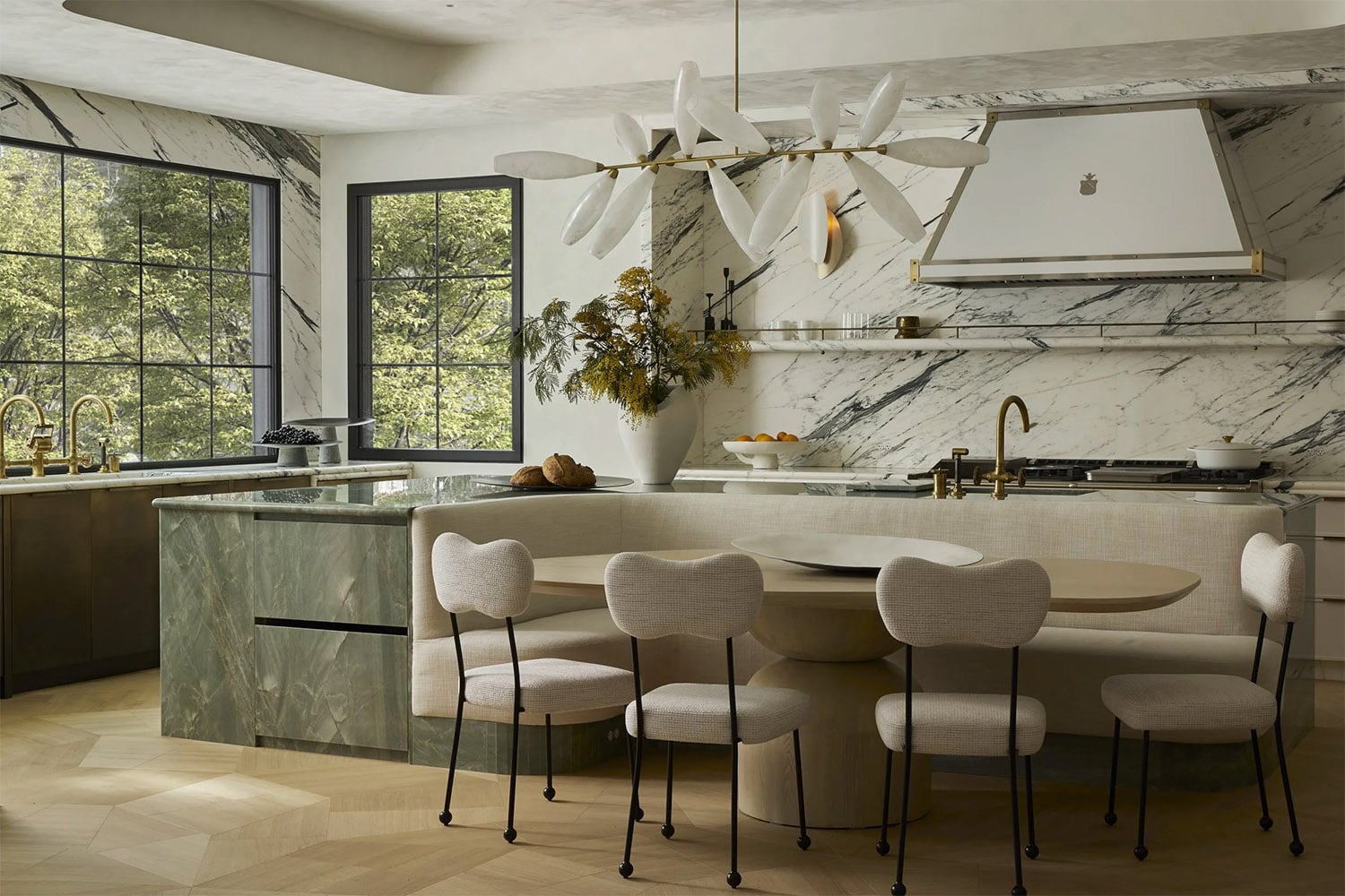 Warm white kitchen with green stone island, open marble shelving, and an island with a built-in dining nook. 