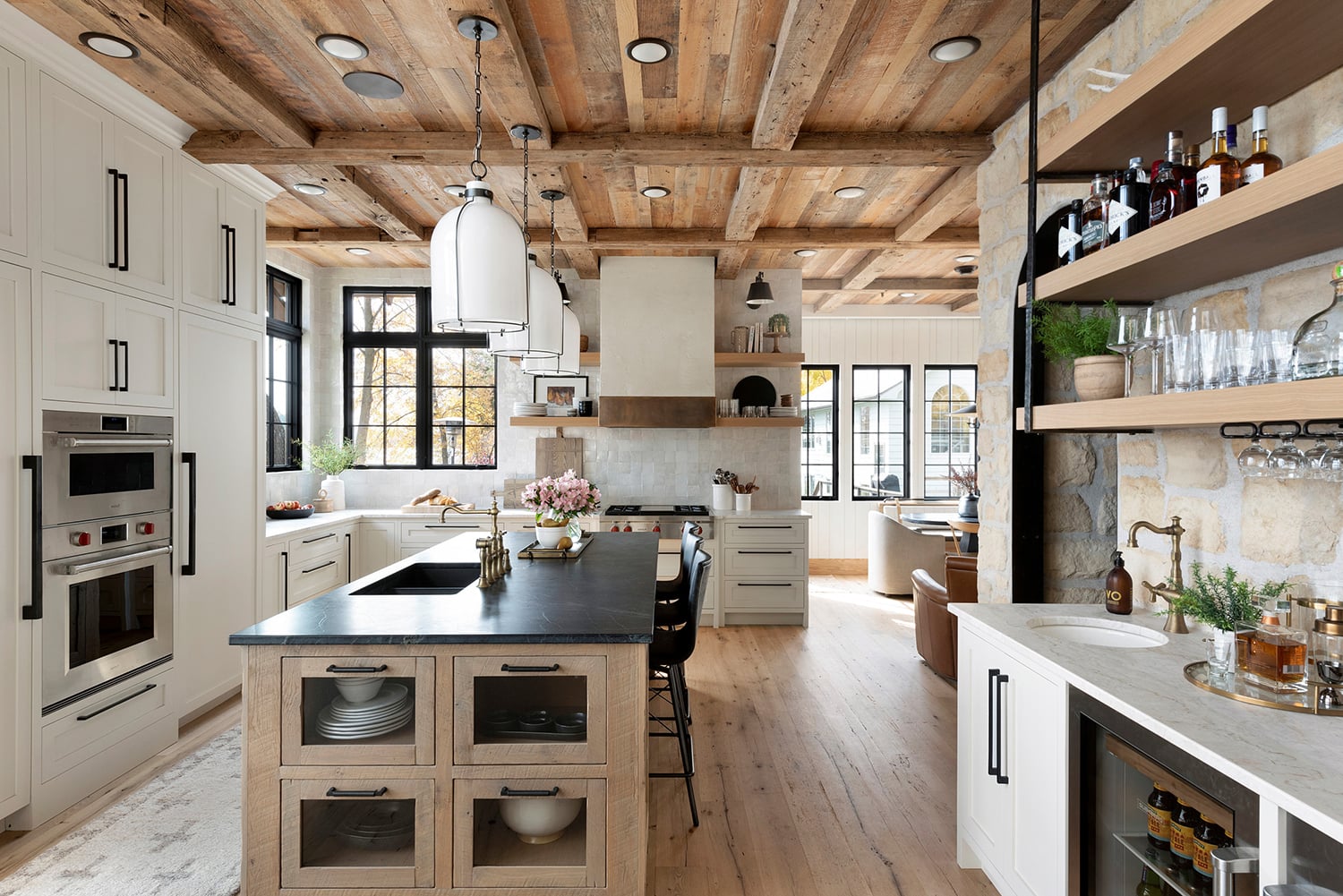 Farmhouse cream kitchen cabinets with matte black hardware light wood floors wood beam ceiling stone accent wall and black countertop island by Tays and Co