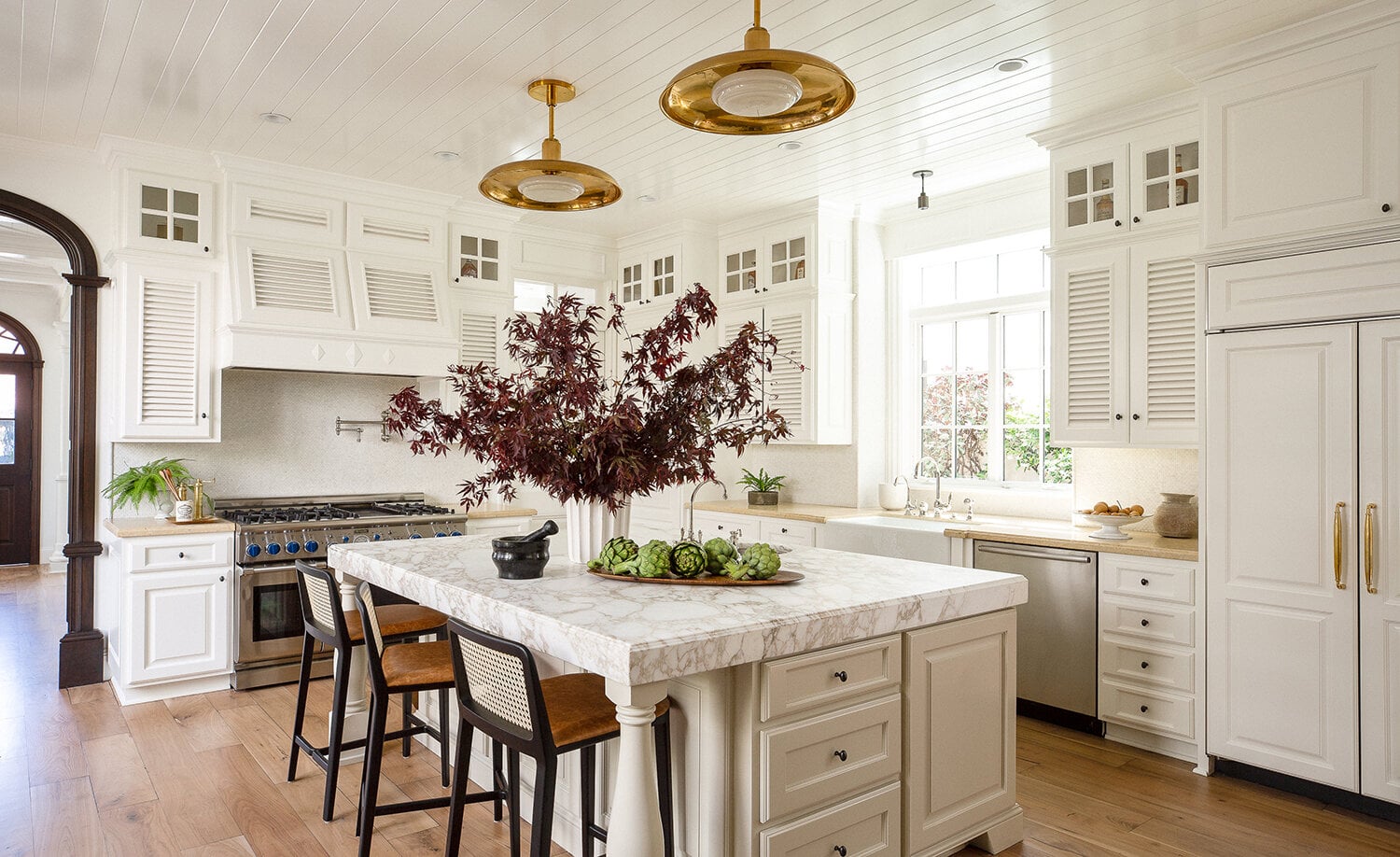 Country kitchen with warm white cabinets, light wood flooring and brass accents.