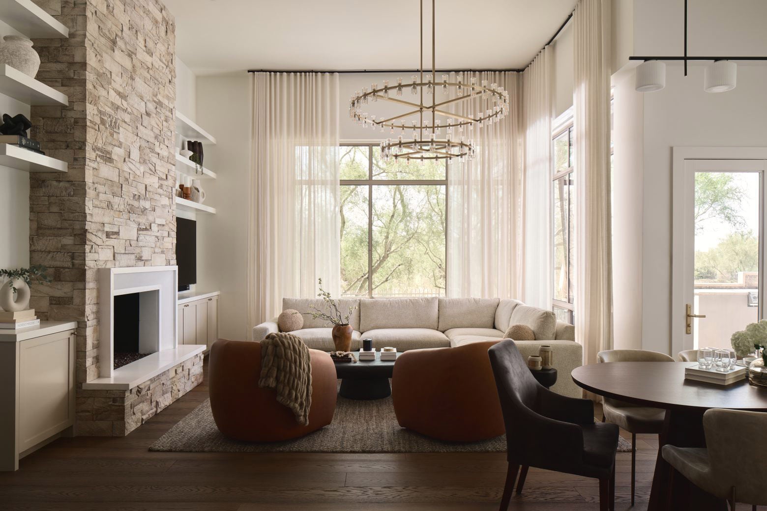 Modern farmhouse living room with brass chandelier, stone fireplace and dark wood flooring.