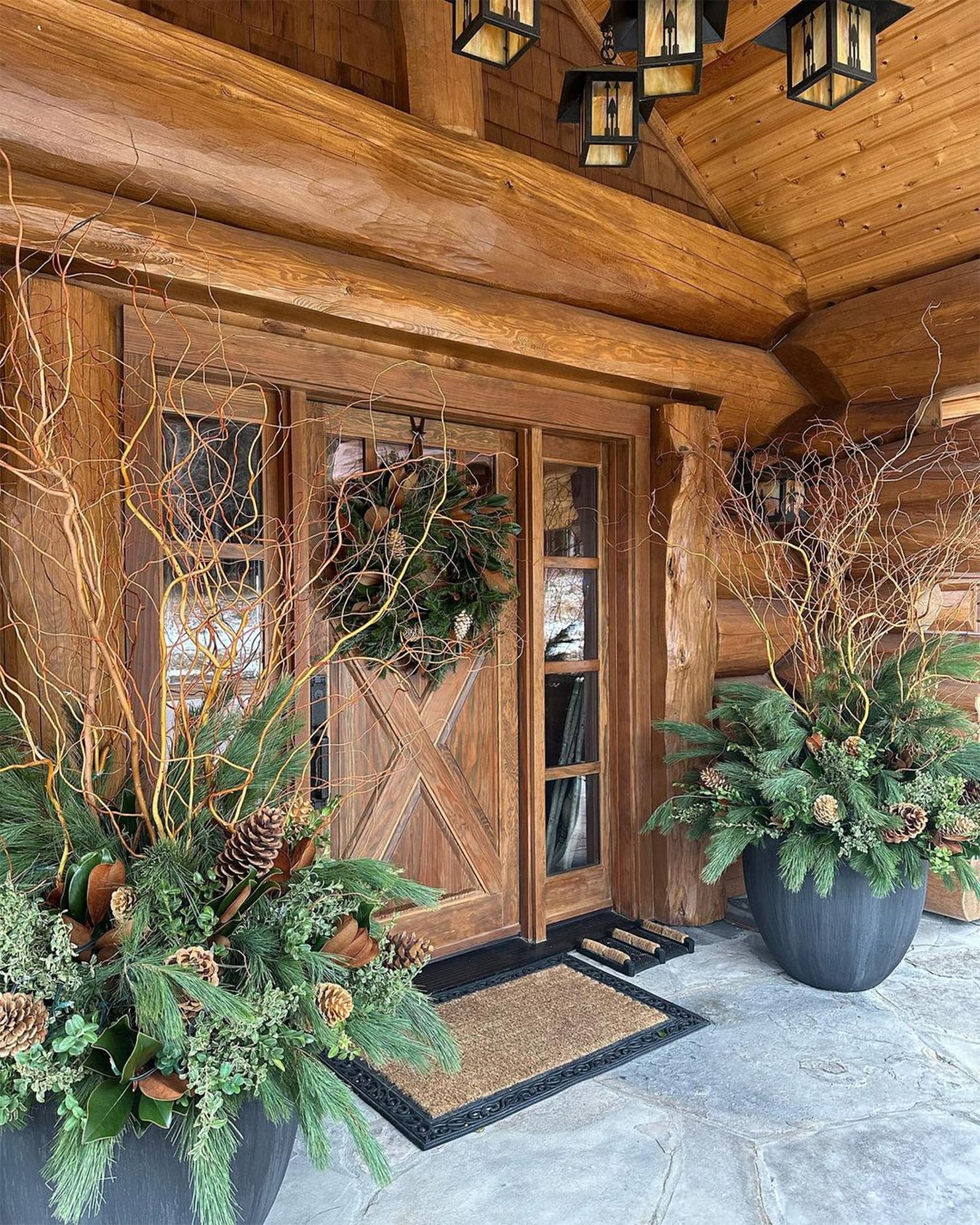 Rustic handcrafted log home outdoor Christmas front porch with winter planters, and a large front door wreath