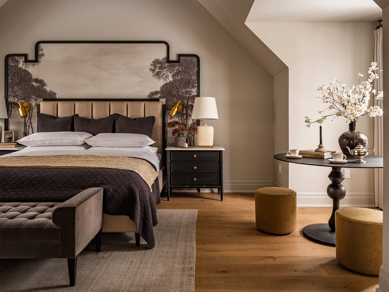 A primary bedroom with warm earth tones including wood flooring, brown bedding and yellow ochre ottomans