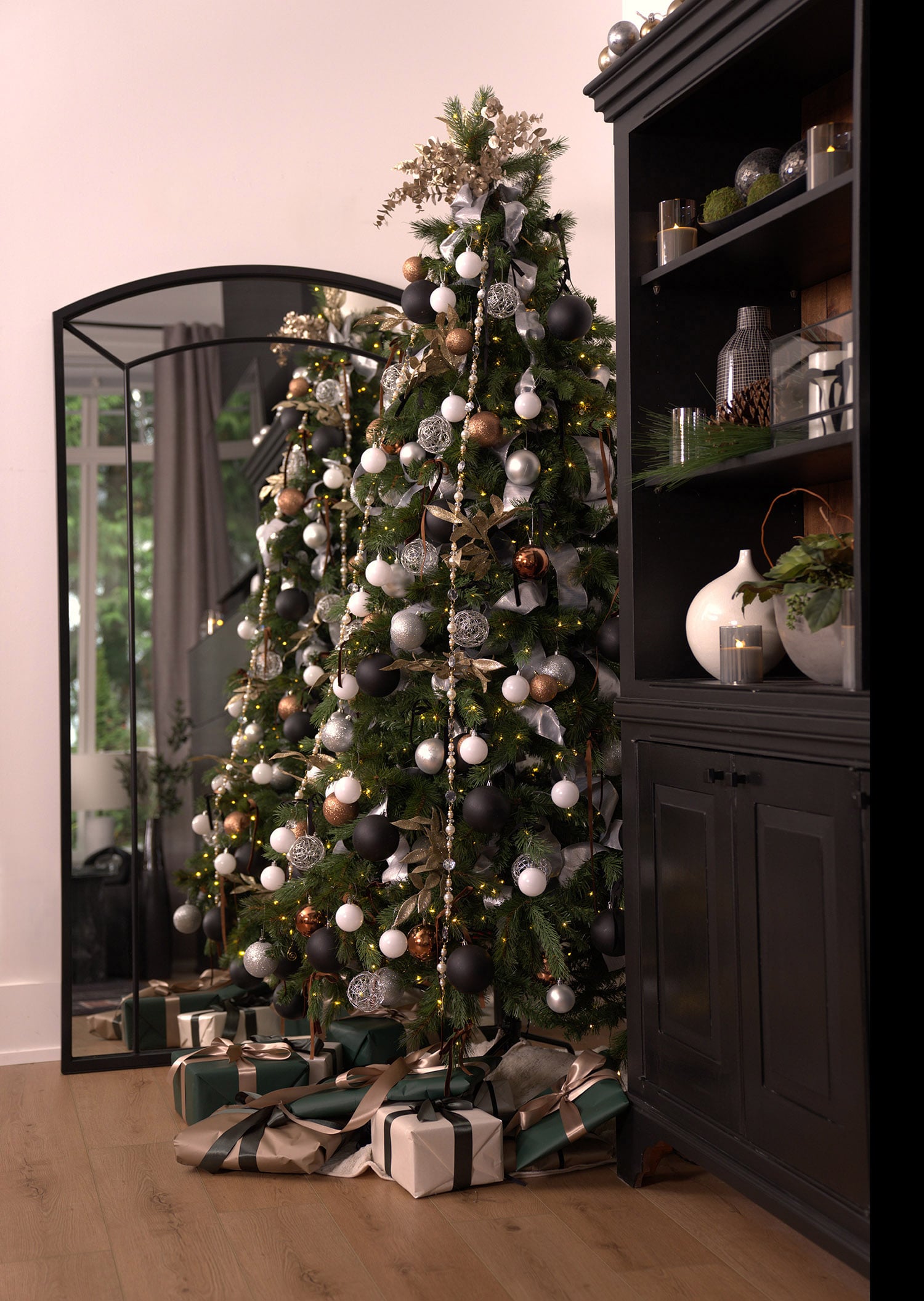 Modern Christmas tree with rose gold black white and silver mesh ornaments black velvet bows and crystal bead draping beside a large mirror