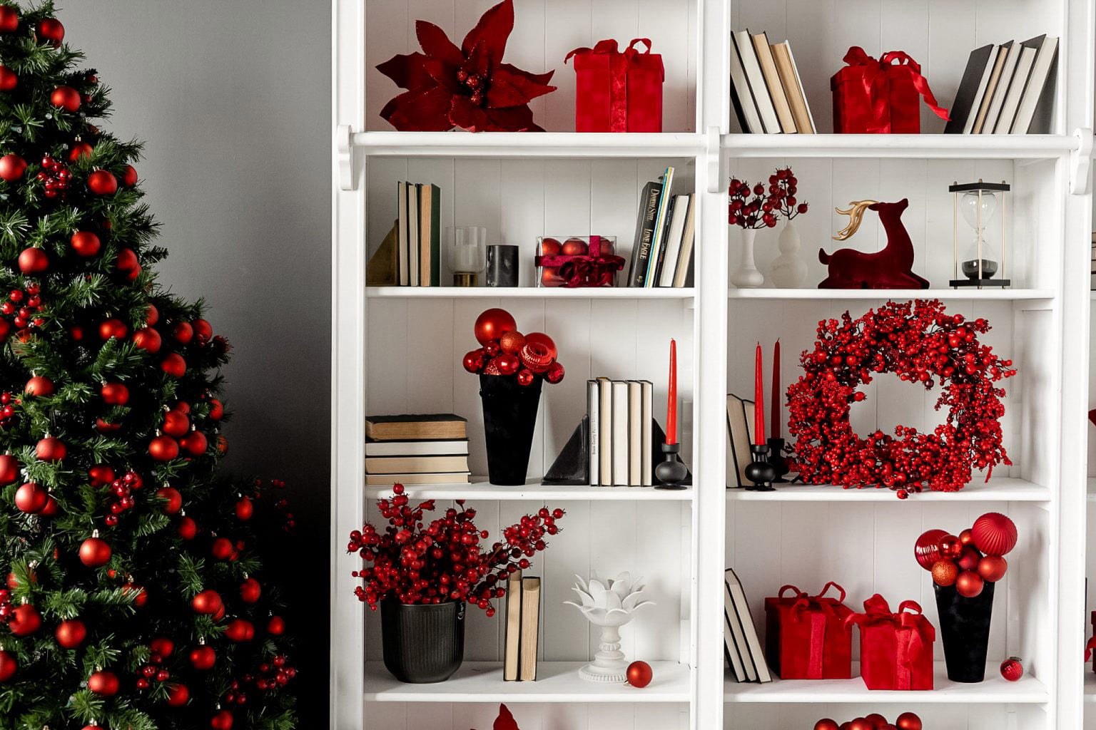 Modern monochromatic red Christmas tree with red ornaments berry clusters and built-in shelving with red poinsettias and candles