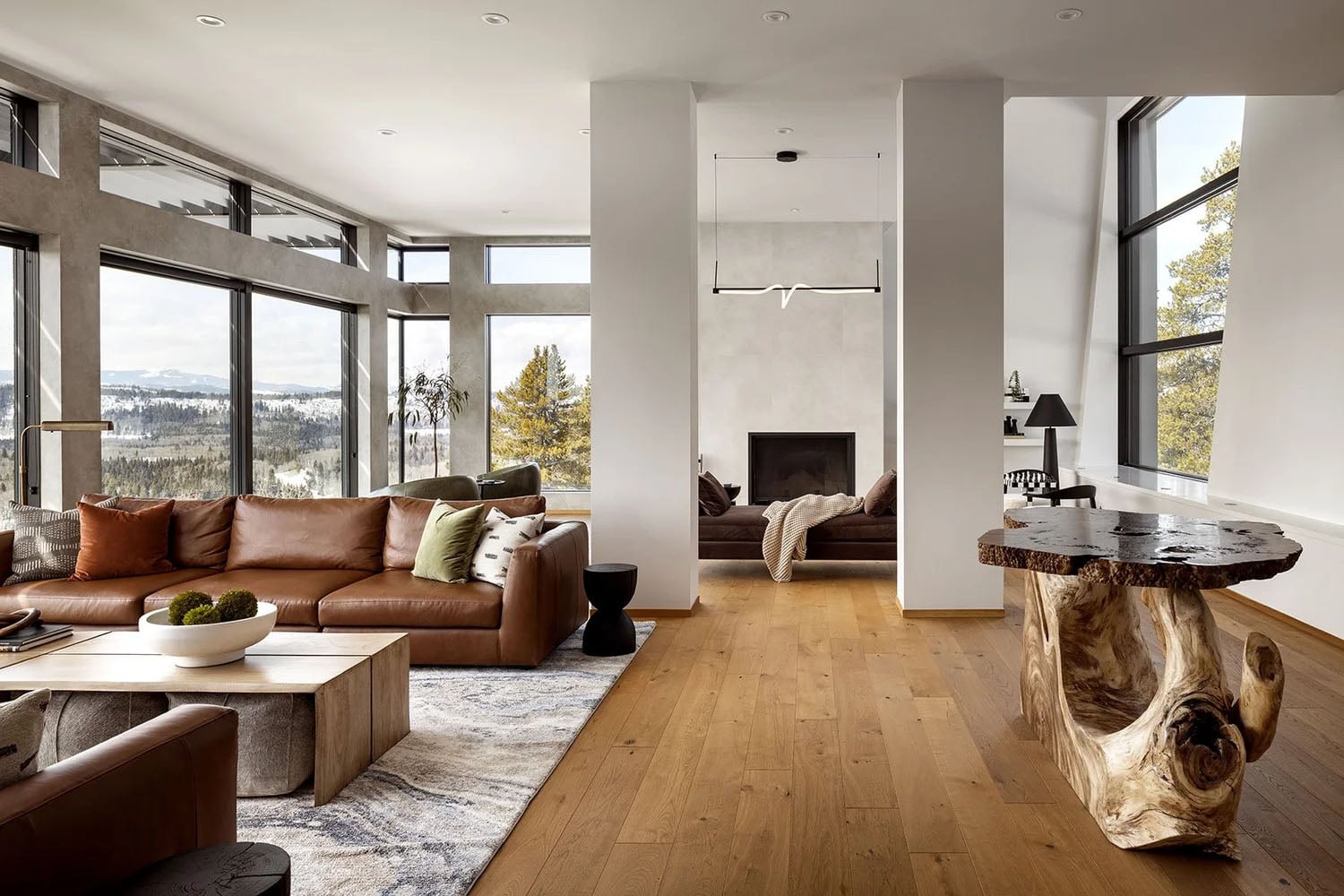 Modern rustic living room with mountain views, warm wood flooring, and leather furniture