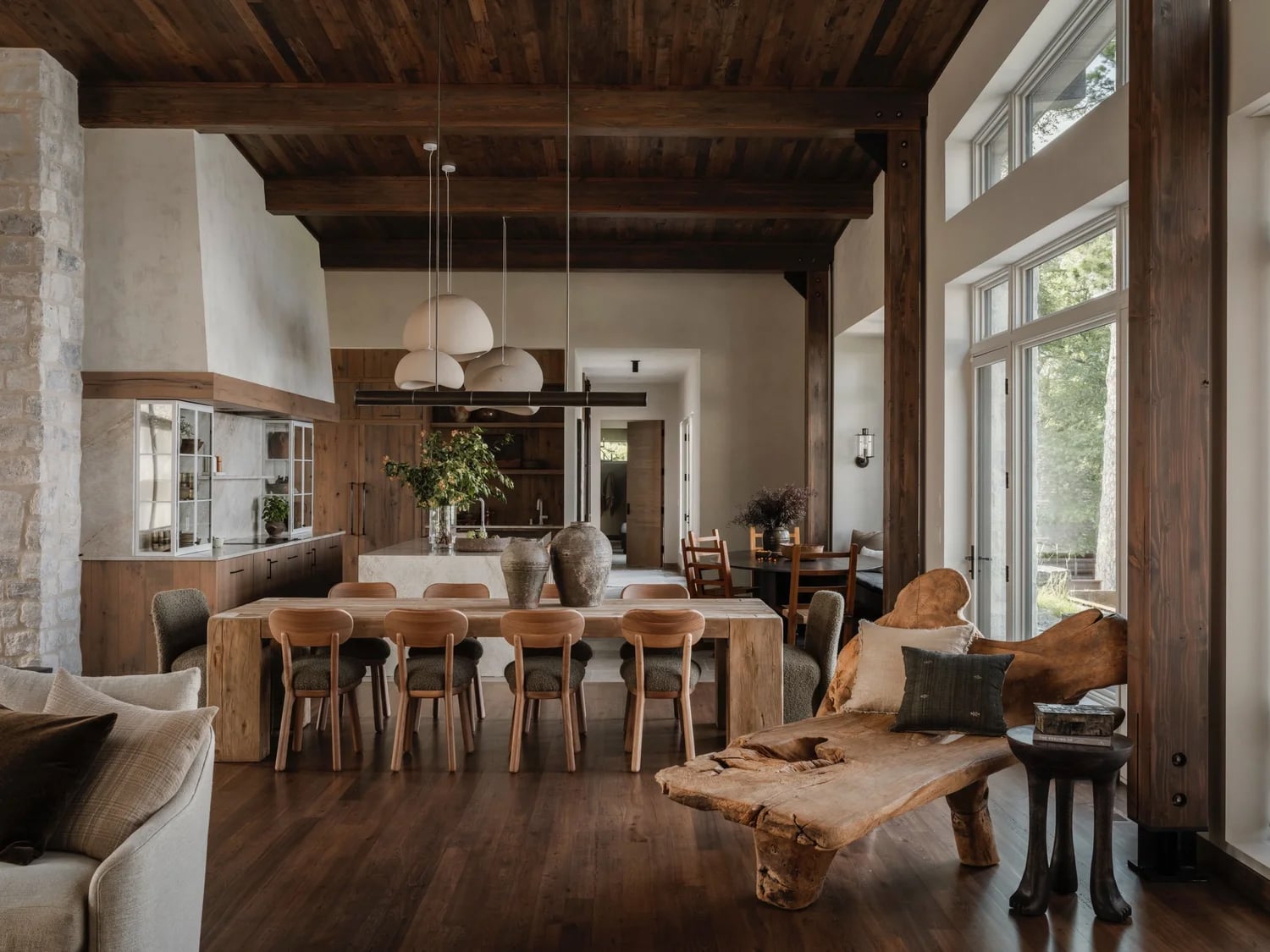 Rustic dining room with dark wood flooring and ceiling beams, light wood table and stone accent wall