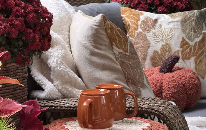 Fall aesthetic outdoor seating with pumpkin pillows, mums, and pumpkin spice coffee