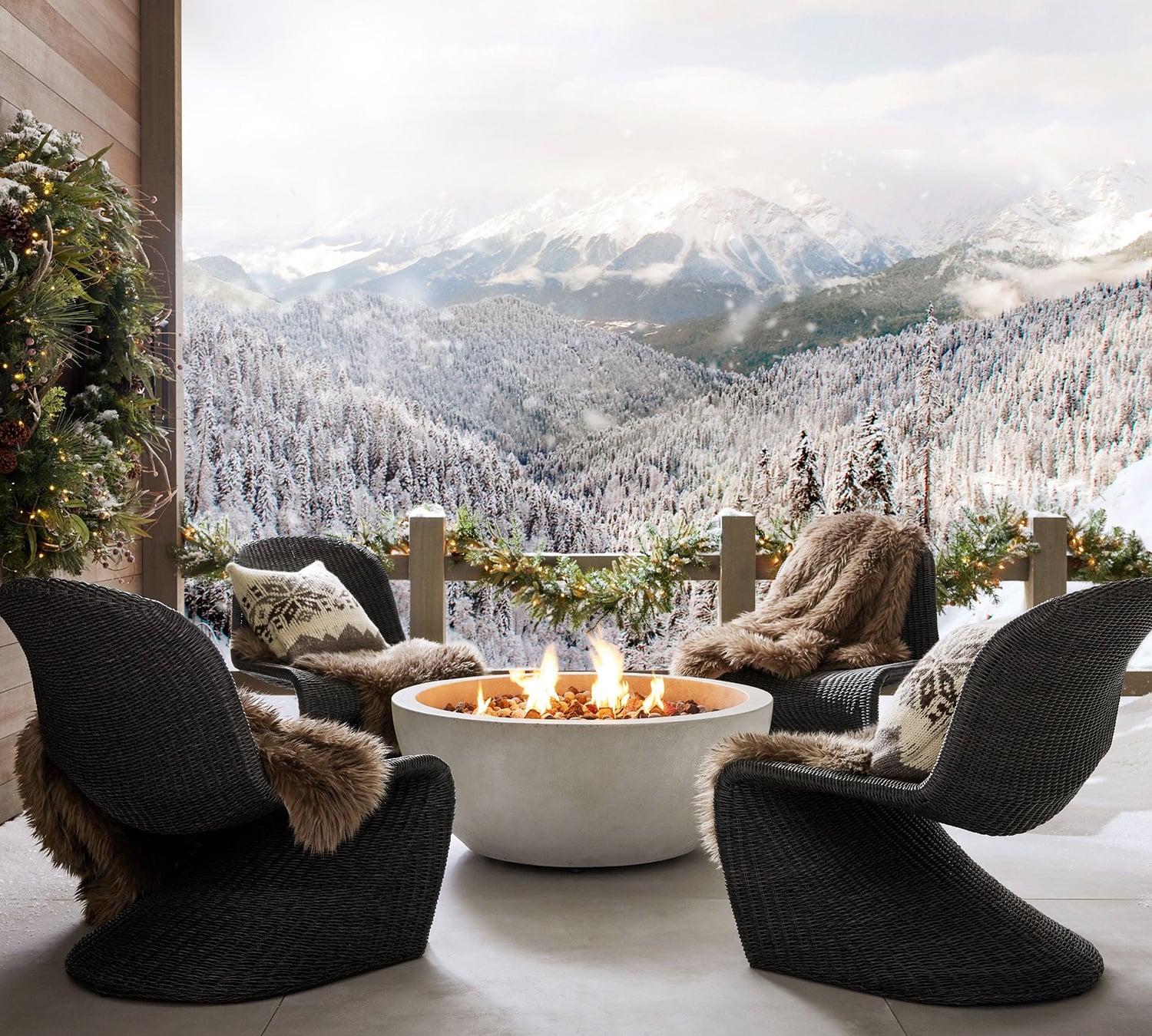 Rustic outdoor deck with wicker chairs, fire pit, faux fur blankets, a wreath and garland
